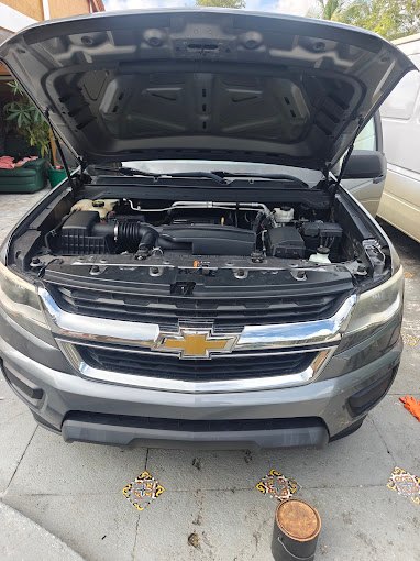 Silver Chevrolet Colorado pickup with the hood open in a driveway, engine bay visible