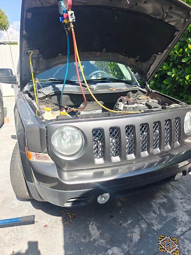 Gray Jeep Patriot with the hood open and blue, red and yellow AC gauge hoses connected