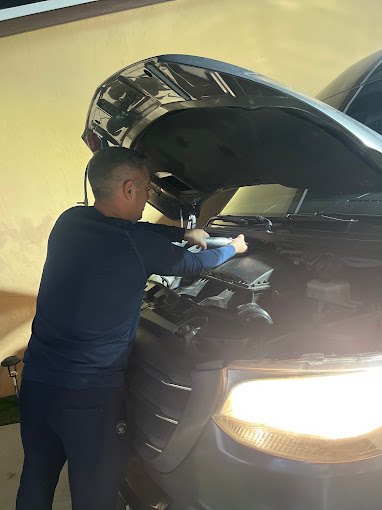 Technician working under the open hood of an SUV in the evening, lit by the headlights